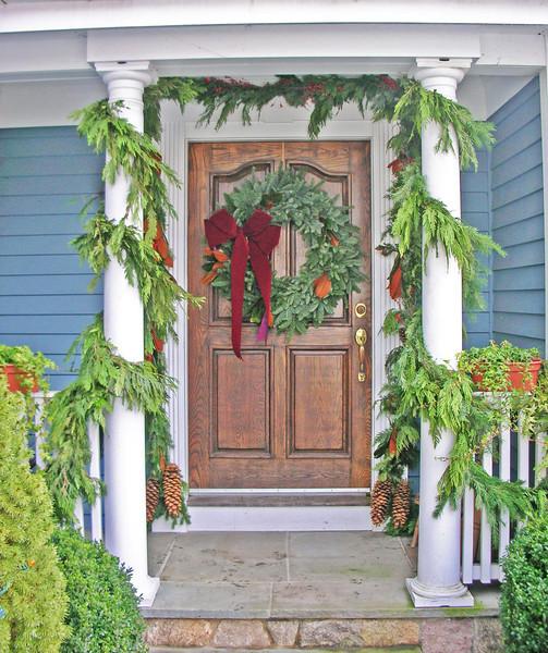 wreath with a bow on exterior door, framed by garland wrapped around railing and pillars