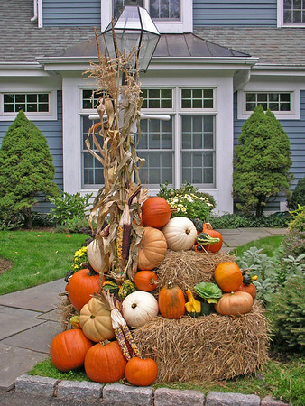pumpkins stacked on hay bales next to lamp post wrapped in dried corn stalks